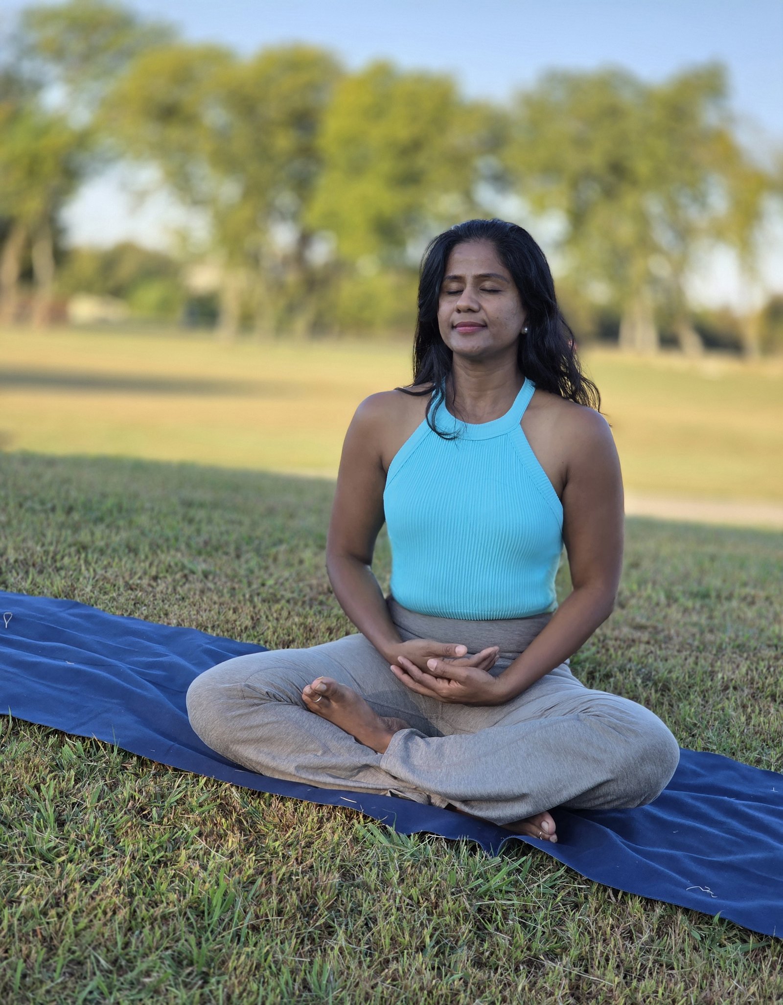 Jhansi meditating outdoors in a blue top